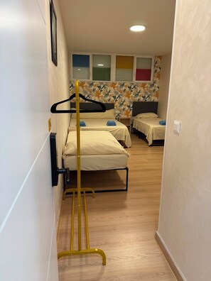A corridor with three beds, a yellow folding chair, and a window with blinds.