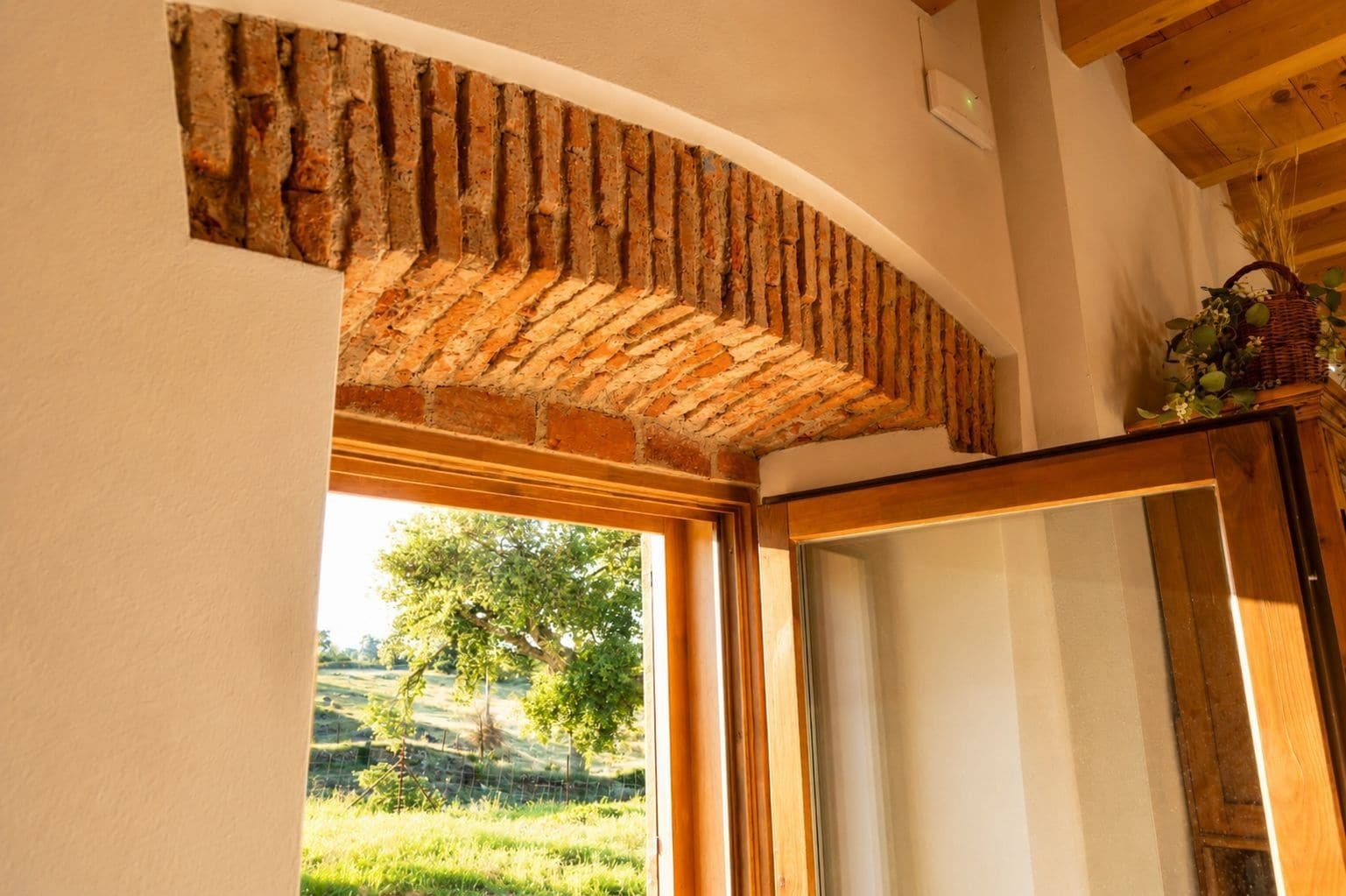 A room with a brick wall, a wooden ceiling, and a view of a green landscape through a window.