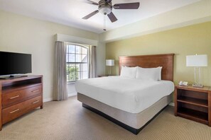 Habitación de hotel con cama, televisor sobre una cómoda de madera, ventilador de techo y ventana con cortinas.