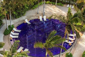 A circular infinity pool with lounge chairs around it, surrounded by palm trees and greenery. - Waikiki | Harborfront Stay | Pool & Marina | Hotel Room (Honolulu)