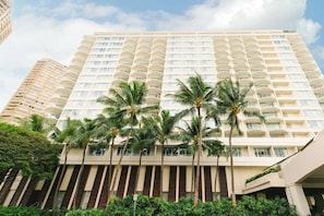 Un hotel de diverses plantes amb balcons, palmeres i un cel serè.