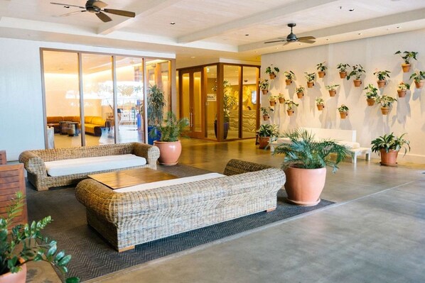 Un vestíbul d'hotel amb una zona de seients, una entrada amb portes de vidre i una paret decorada amb plantes en testos.