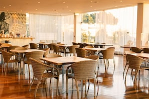 Un vaste espace de restauration intérieur, doté de chaises et de tables en osier, de grandes fenêtres et d’un aménagement intérieur moderne.