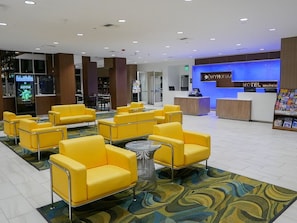 Eine Hotelhalle mit gelben Sitzgelegenheiten, einem Empfangsbereich und einem Teppichboden.