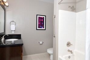 Bagno con lavabo su piano nero, water, quadro incorniciato al muro e doccia con maniglione.