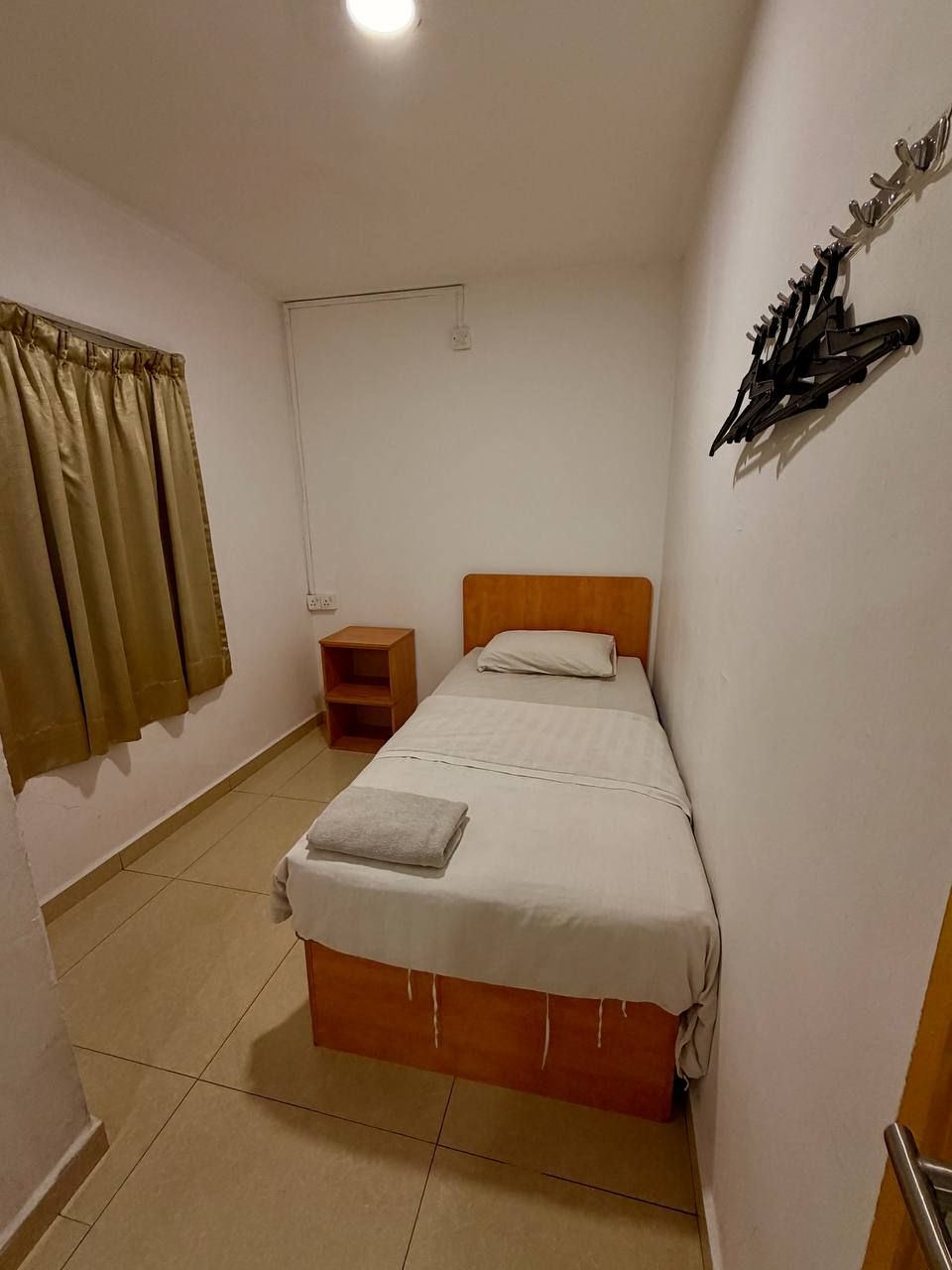 Una habitación pequeña con una cama individual, cabecera de madera, mesita de noche y cortina.