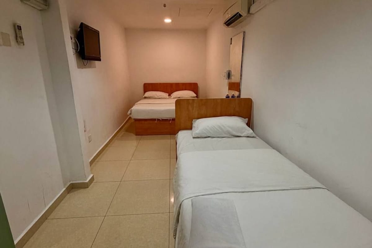 A narrow hotel room with two single beds, a small television, and a tiled floor.
