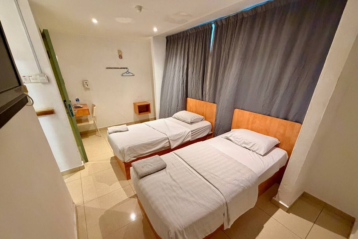 A hotel room with two beds, a small desk, a chair, and a window with curtains.
