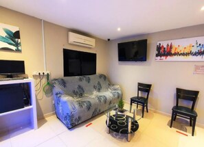 Sala de estar com sofá, cadeiras, mesa de centro, televisão e obras de arte nas paredes.