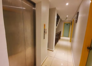 Um corredor com elevador de metal, escada e uma porta no final.