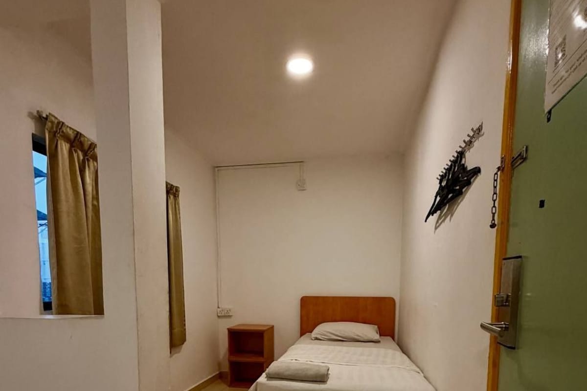 A single-bed room with a wooden headboard, a small bedside table, and a window with curtains.