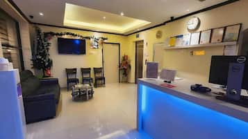 Un área de recepción con un mostrador, sillas, un televisor y un reloj en la pared.