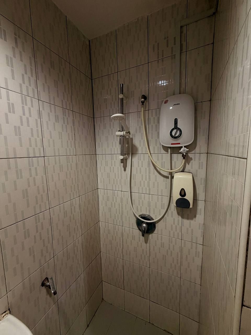 A bathroom with a shower, a toilet, and a hand dryer mounted on the wall.