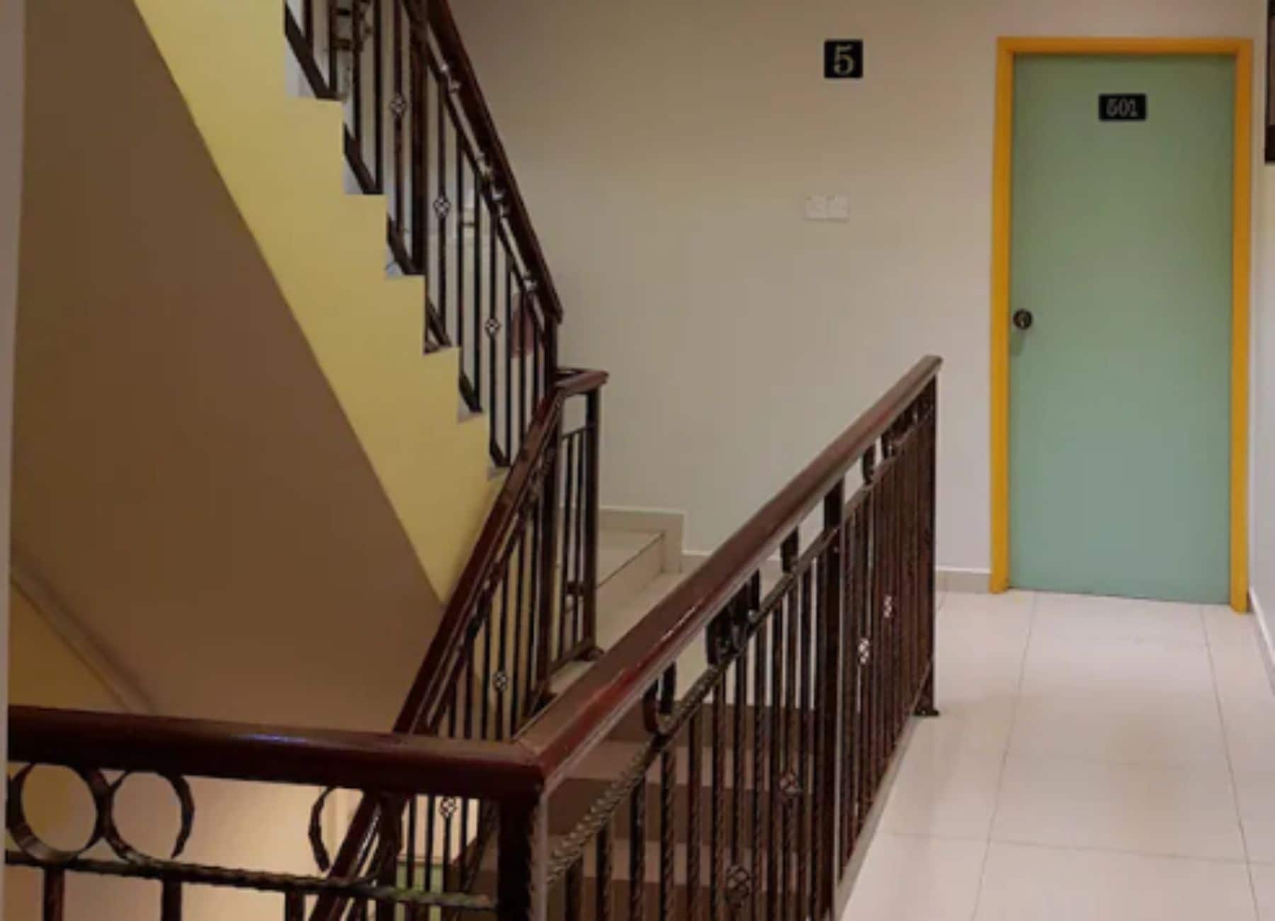 Una escalera con barandilla de madera y balaustradas metálicas, que lleva a una puerta marcada con el número 5.