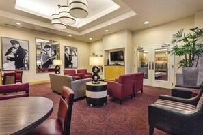 Eine Hotellobby mit rotem Teppich, Sitzgelegenheiten in Rot und Beige sowie einem Fernseher und gerahmten Bildern an den Wänden.