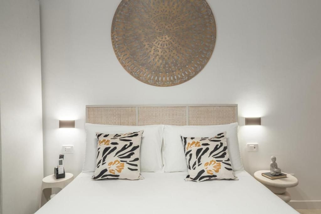 Een opgemaakt bed met gestreepte kussens, een decoratief kunstwerk aan de muur en bedlampjes.
