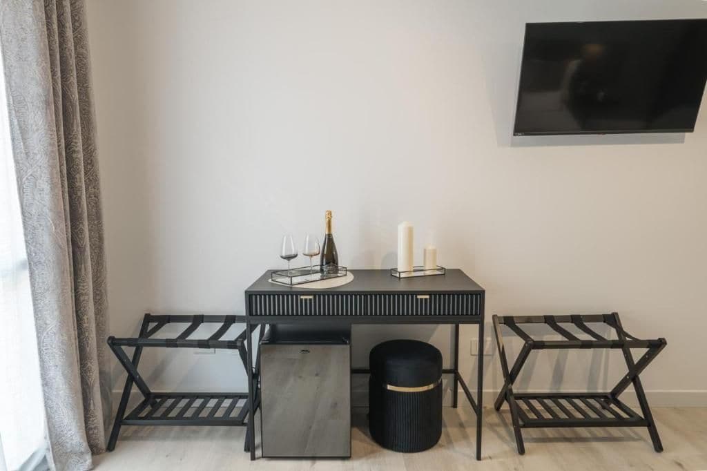 Una habitación moderna con una mesa negra, dos sillas negras, un bote de basura negro y un televisor montado en la pared.