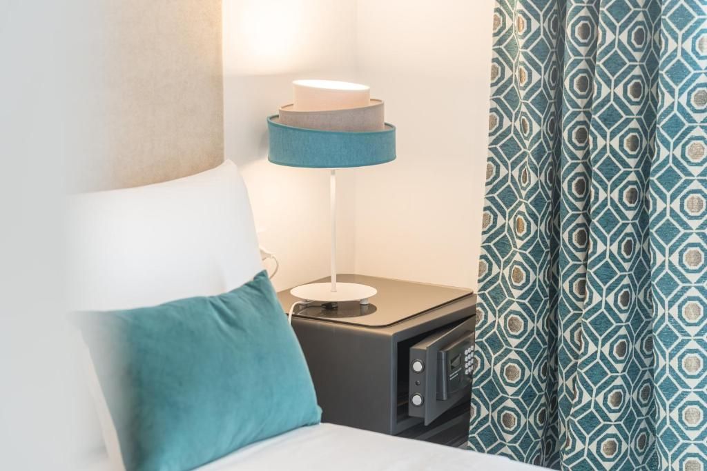 A hotel room with a bed, a bedside table with a lamp, and a patterned curtain.