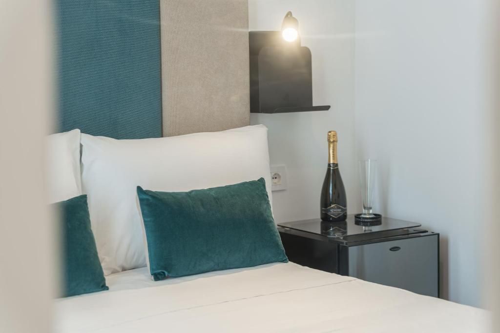A hotel room with a bed, two pillows, a nightstand, a bottle of champagne, and a wall-mounted light.