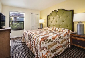 Quarto de hotel com cama, escrivaninha, luminária, telefone e janela com persianas.