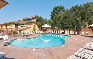 Piscina com espreguiçadeiras e guarda-sóis, cercada por um muro de madeira e árvores.