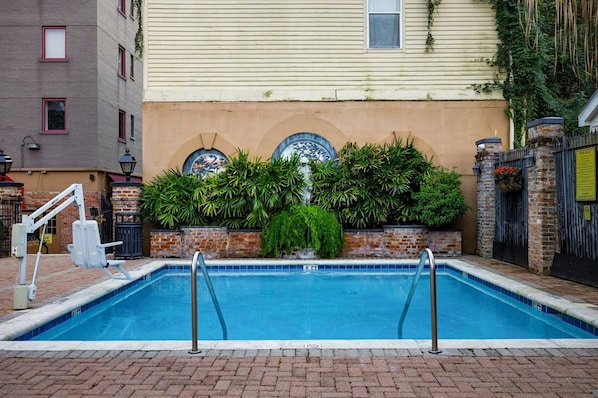 Una piscina con borde de ladrillo, escalera metálica y pared con plantas y un revestimiento decorativo.