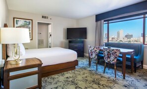 Habitación de hotel con cama, televisión, escritorio y silla, y vista a la ciudad.