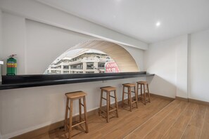 Un interior moderno con una encimera negra, tres taburetes de madera y vistas a un edificio a través de una ventana semicircular.