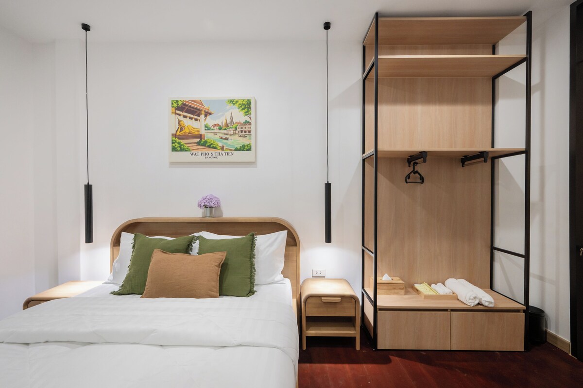 Una habitación de hotel moderna con una cama, una mesita de noche, una pequeña mesa, un armario de madera y un cartel en la pared.