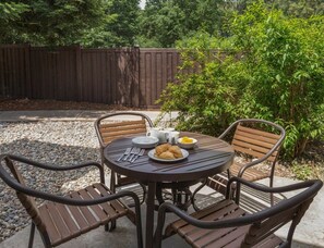 An outdoor patio with a round table and four chairs, surrounded by gravel and a wooden fence. - Bass Lake | Group Lake Getaway | Pool + Lake | 2BR (Bass Lake)