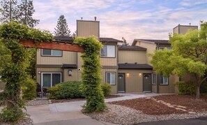 A multi-story residential building with a modern design, featuring a mix of wood and metal siding, a covered patio, and a landscaped front yard with trees and shrubs. - Bass Lake | Group Lake Getaway | Pool + Lake | 2BR (Bass Lake)