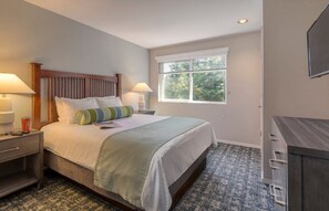 A bedroom with a bed, two bedside tables, a nightstand, a dresser, and a window with a view of trees. - Bass Lake | Group Lake Getaway | Pool + Lake | 2BR (Bass Lake)