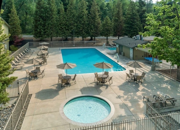 Una piscina rectangular amb gandules i ombrel·les, envoltada d'arbres i una zona tancada per una tanca.