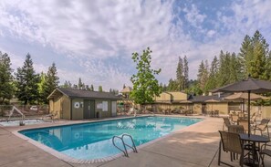 A swimming pool with lounge chairs and umbrellas, surrounded by trees and a building with a sign. - Bass Lake | Group Lake Getaway | Pool + Lake | 2BR (Bass Lake)
