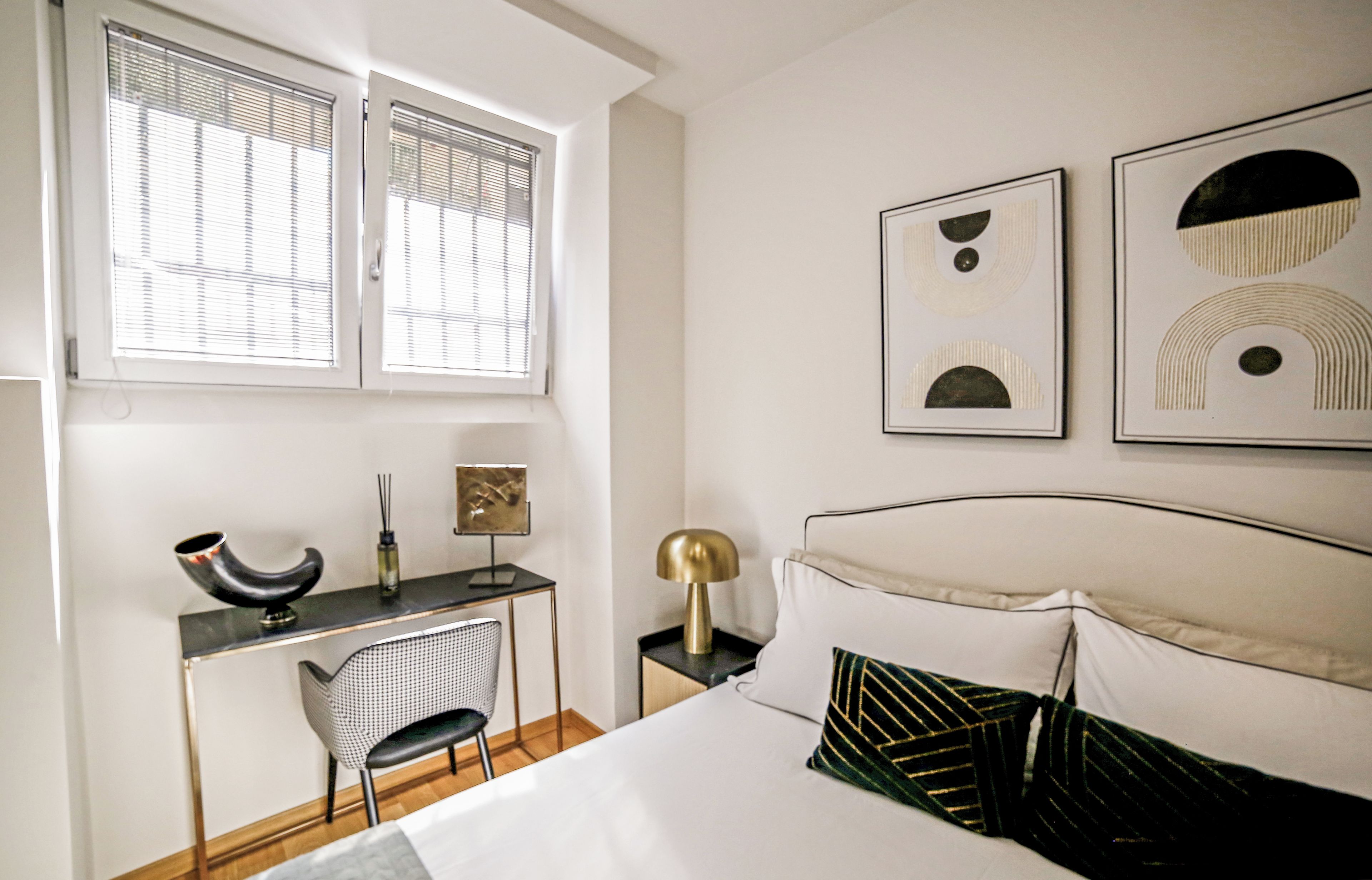 A bedroom with a bed, a desk, a chair, and two wall-mounted artworks.