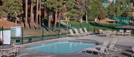 Une piscine dotée de chaises longues et d’un espace délimité par une clôture, le tout entouré d’arbres.