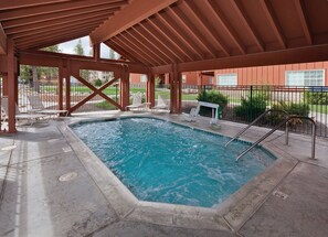 A covered swimming pool with a wooden deck, lounge chairs, and a small seating area. - Big Bear | Family Summit Stay | Pool + Hot Tub | 2BR Condo (Big Bear Lake)
