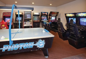 Une pièce équipée d’une table de billard, de jeux d’arcade et d’un espace détente avec des sièges.