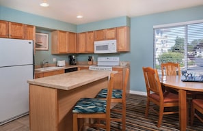 A compact kitchen with wooden cabinets, a microwave, a stove, and a dining area with a table and chairs.