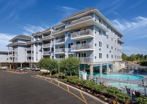 A multi-story hotel with balconies, a swimming pool, and a parking lot.