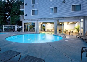 A swimming pool with lounge chairs, a bar area, and a building with multiple windows.