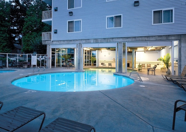 A swimming pool with lounge chairs, a bar area, and a building with multiple windows.