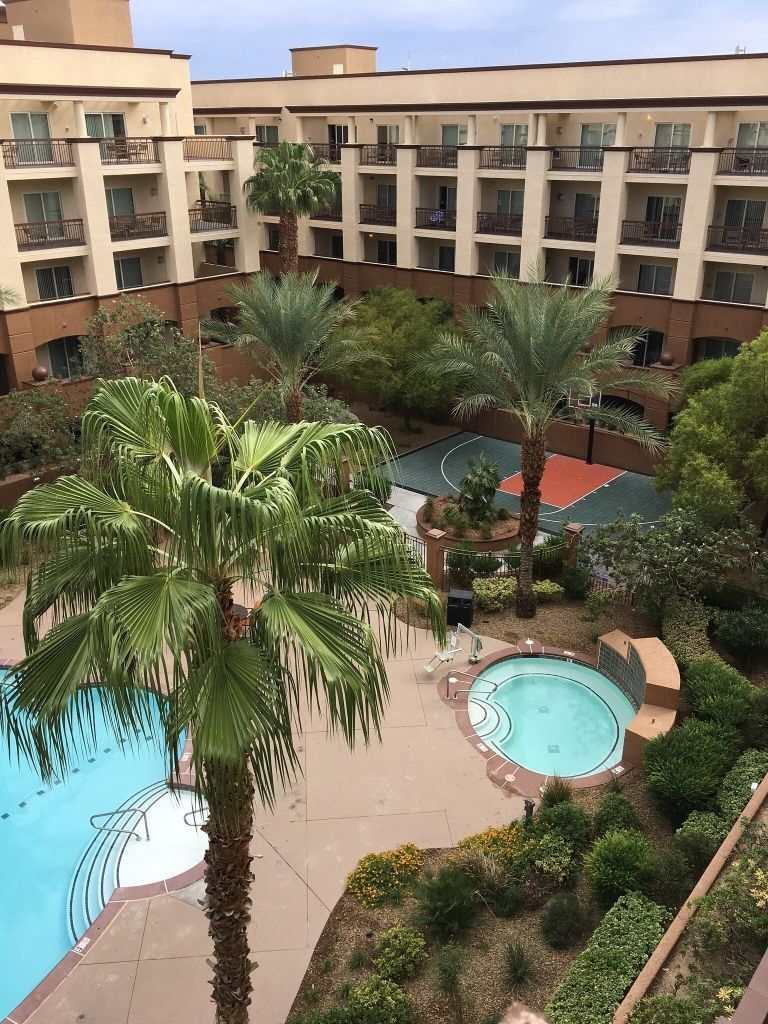 A multi-story hotel with a swimming pool, palm trees, and a basketball court.