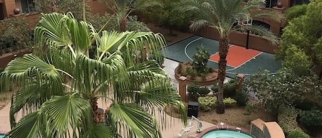 A multi-story hotel with a swimming pool, palm trees, and a basketball court.