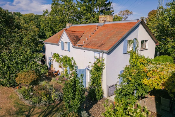 Ein zweistöckiges Haus mit rotem Ziegeldach, umgeben von üppigem Grün und Bäumen.