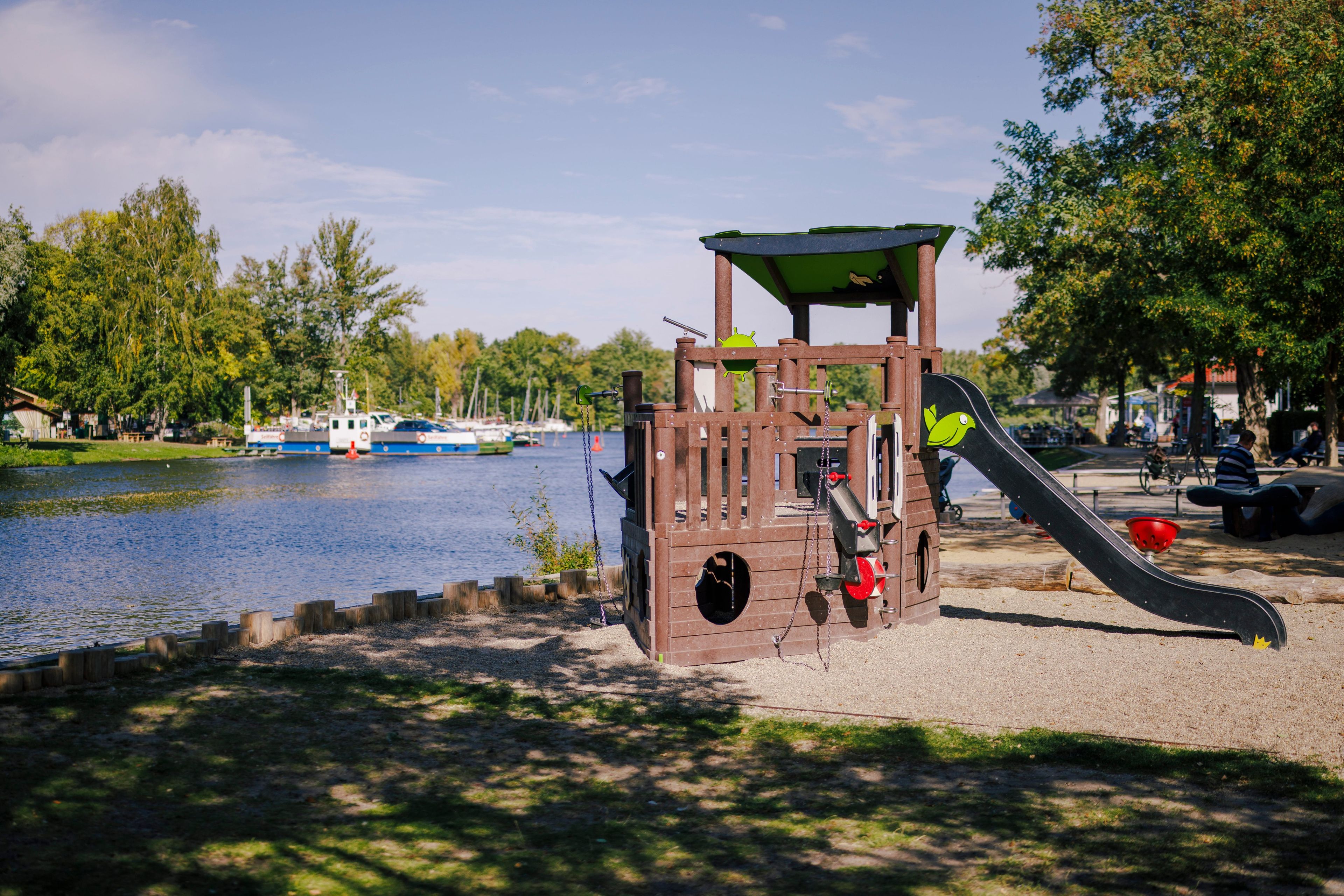 Un parque infantil con tobogán y estructura para escalar cerca de un cuerpo de agua.