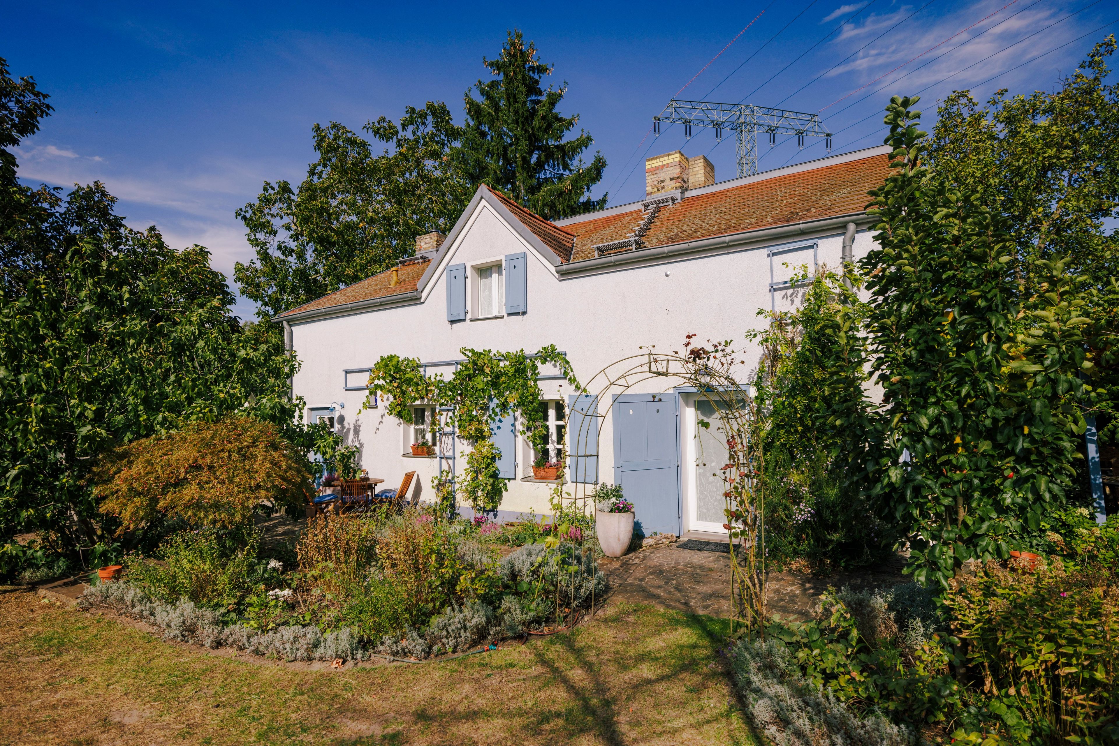 A two-story house with a white exterior, a brick chimney, and a garden with various plants and a small pond.