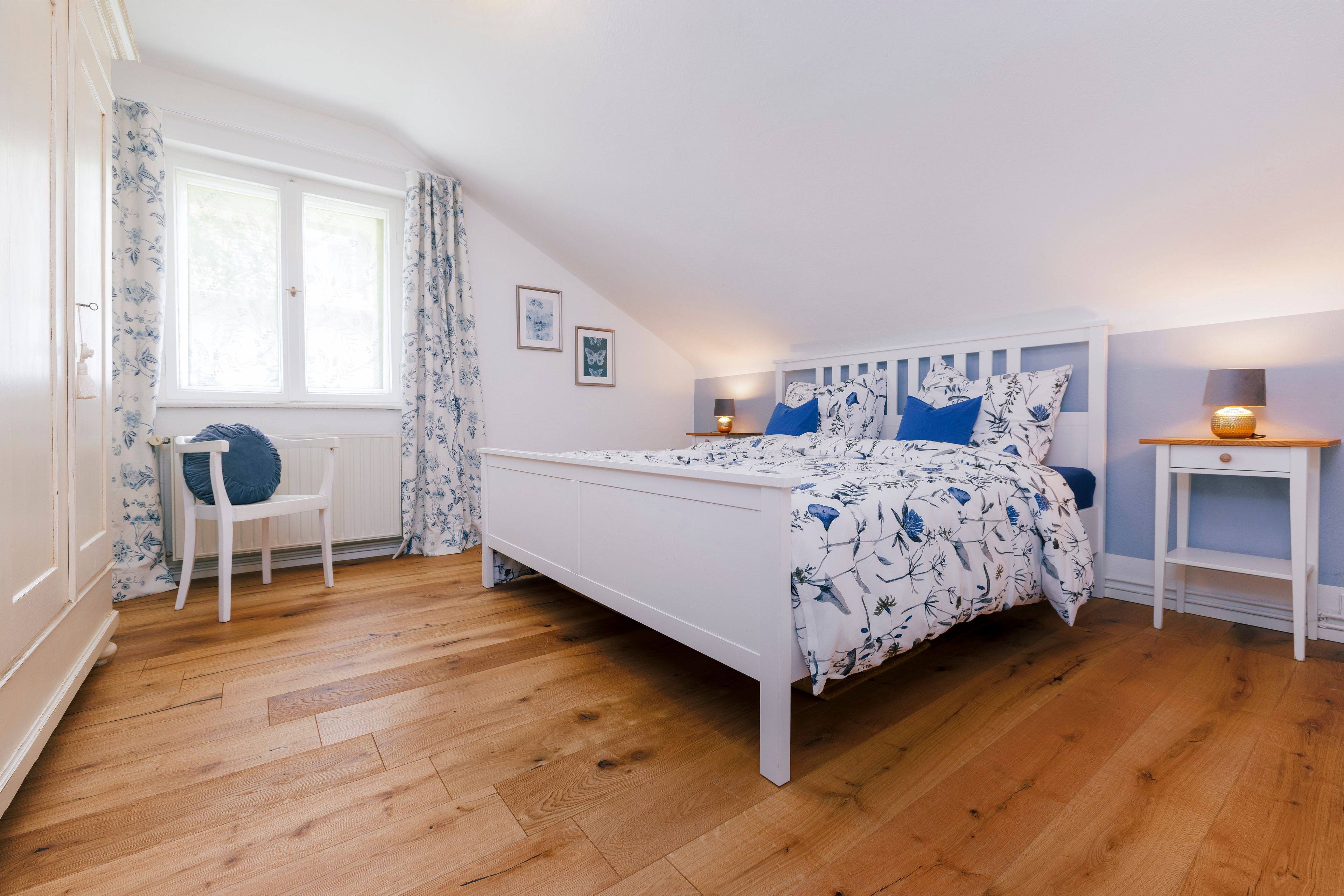 A bedroom with a bed, a chair, a nightstand, and a window with curtains.