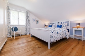 Ein Schlafzimmer mit einem Bett, einem Sessel, einem Nachttisch und einem Fenster mit Vorhängen.