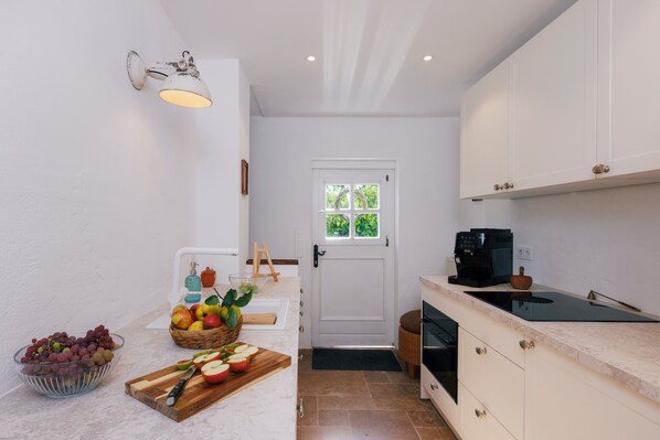 A compact kitchen with white cabinetry, a built-in stove, and a coffee machine.
